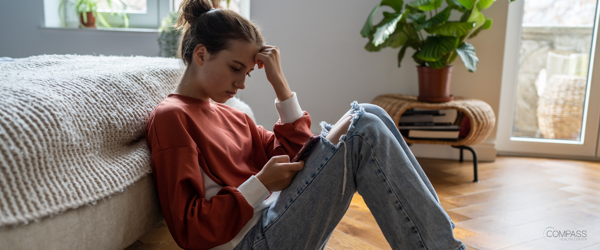 Teen girl sitting on floor sad, looking at the phone 